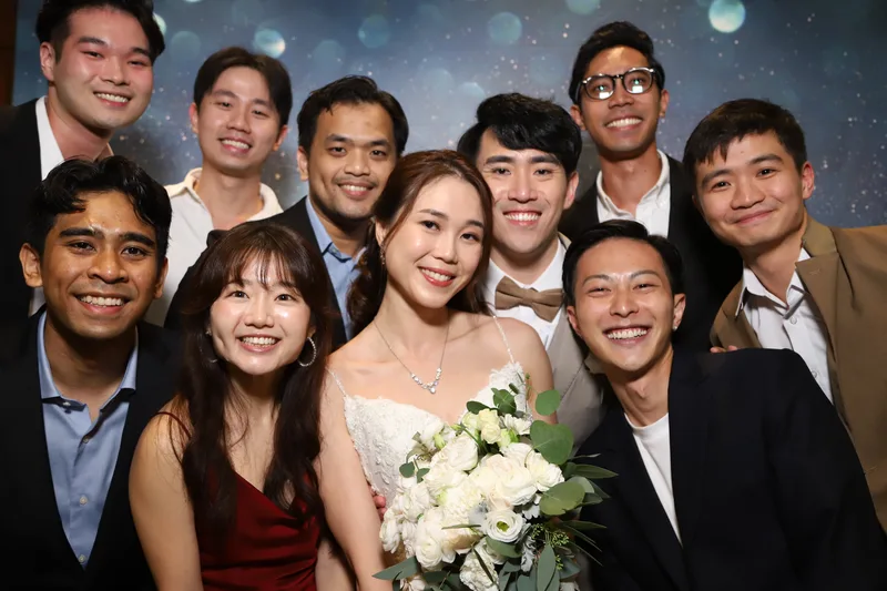 Large group of wedding guests and the bride smiling together at a photo booth with a starry backdrop